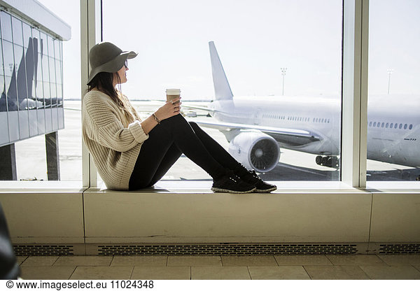 Young woman holding disposable coffee cup and waiting at airport