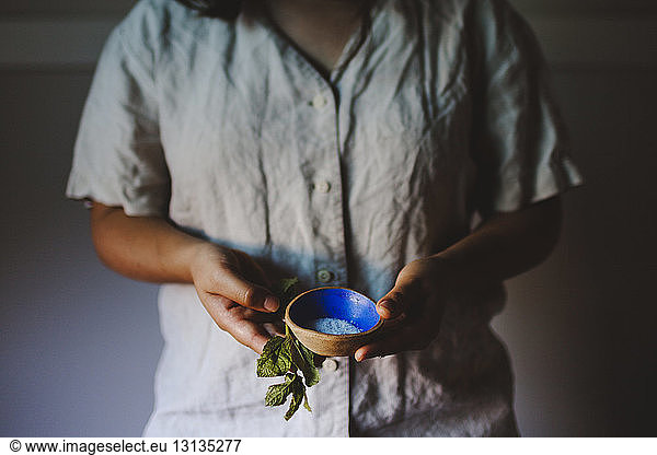 Young woman holding mint leaves and salt bowl at home