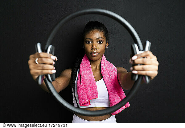 Young woman holding pilates ring in front of black background