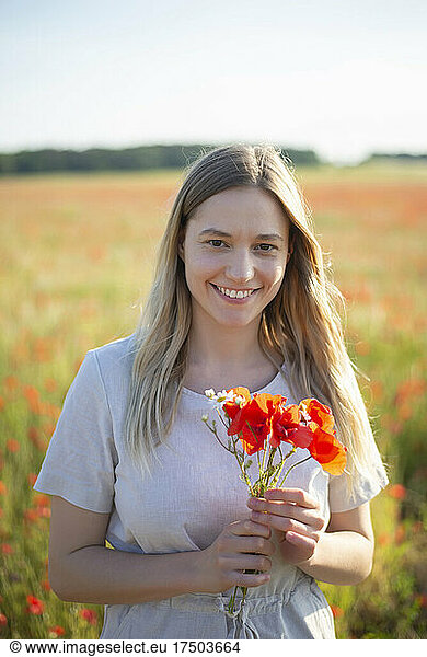 Young woman holding poppy flowers at field