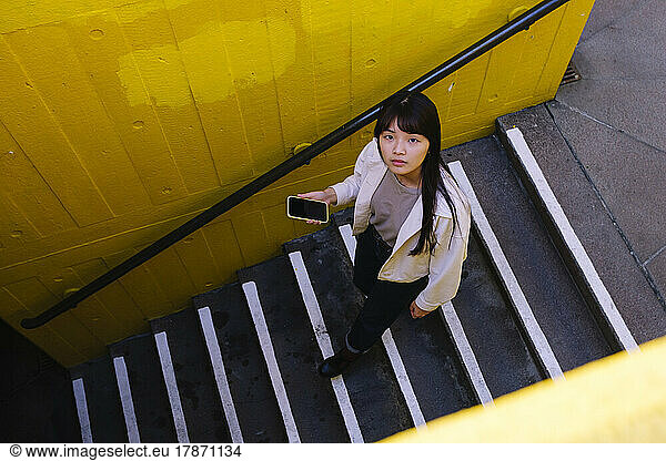 Young woman holding smart phone moving down on steps