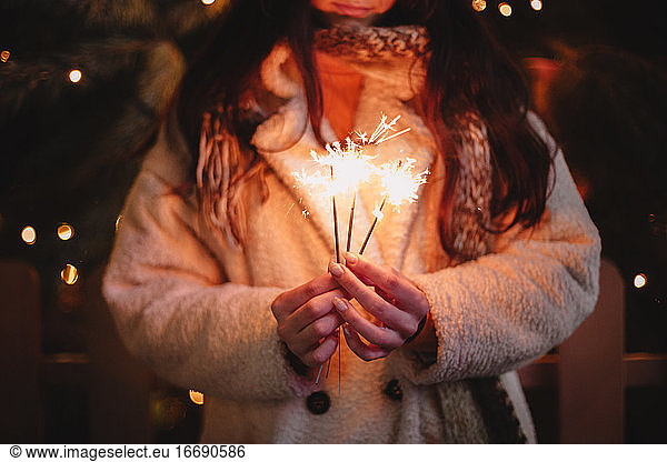 Young woman holding sparklers standing by Christmas tree in city