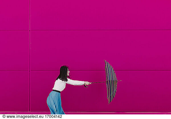 Young woman holding umbrella in front of a pink wall