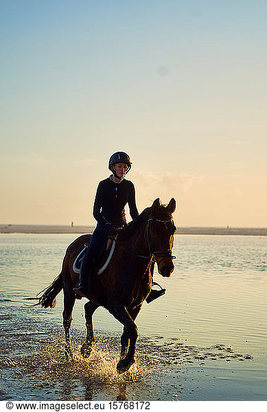 Young woman horseback riding in ocean surf