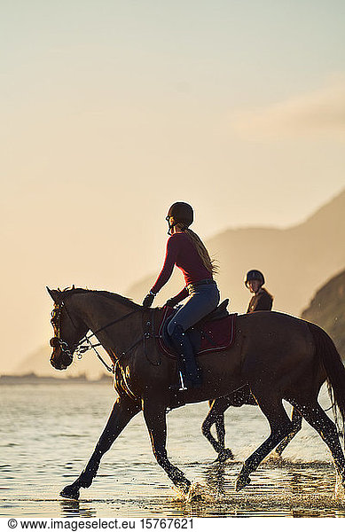 Young woman horseback riding on ocean beach at sunset