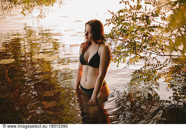 Young woman in a bikini standing in water at sunset