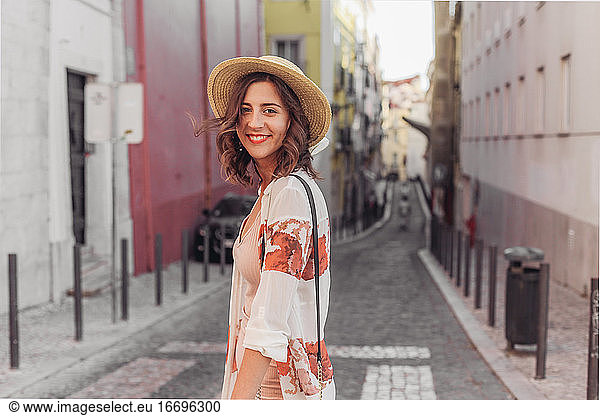 Young woman in a hat smiling and walking on a small street of Europe