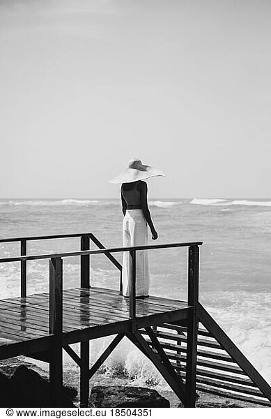 Young woman in a straw hat on the pier  ocean waves splashing.