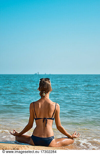 Young woman in a swimsuit sits in a meditative pose on the seashore