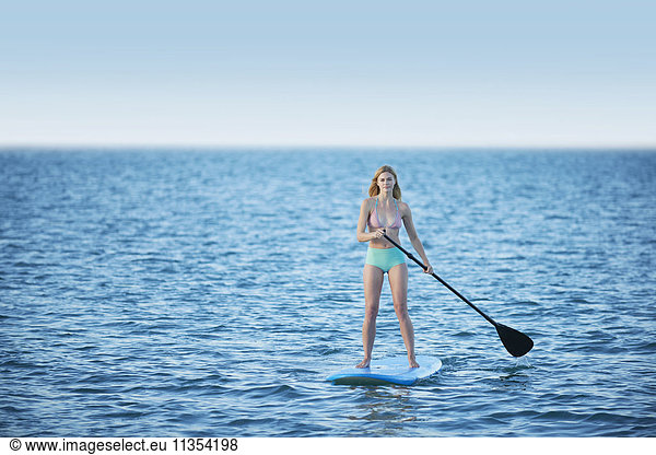 Young woman in bikini paddleboarding on summer ocean