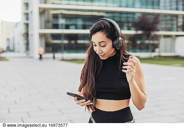 Young woman in black with headphones looking at her smartphone