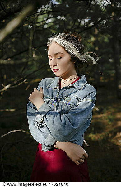 Young woman in denim jacket standing in nature on sunny day