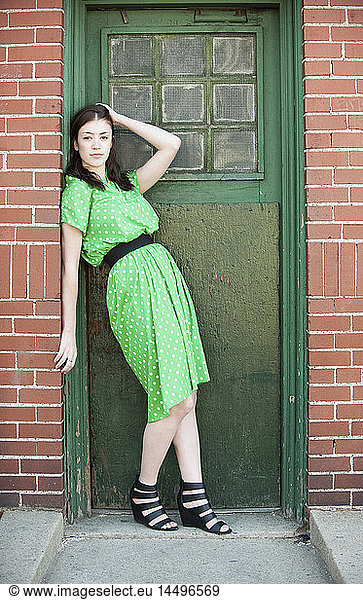 Young Woman in Green Dress with Polka Dots Standing in Doorway with Hand on Head  Portrait