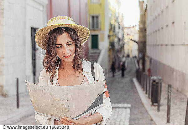 Young woman in hat looking at a map on a small street of European town