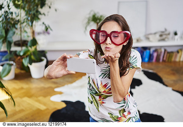 Young woman in heart-shaped glasses taking selfie