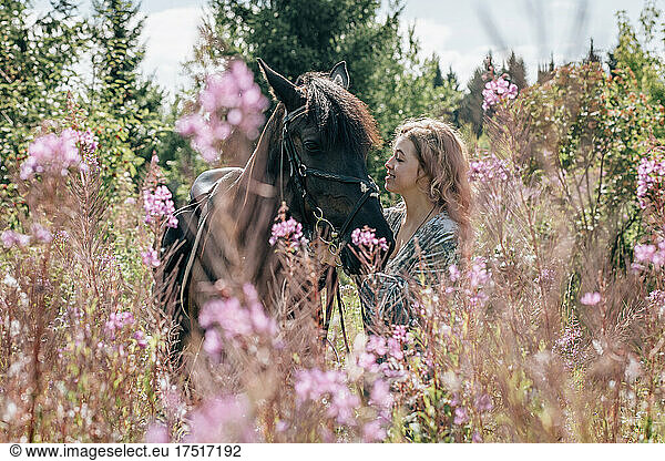 Young woman in meadow in flowers stroking horse.