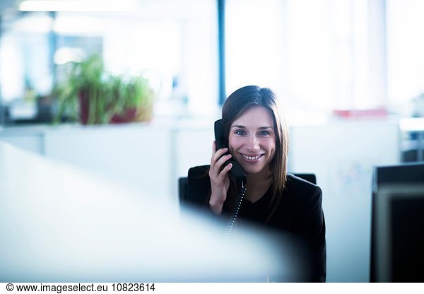 Young woman in office using telephone looking at camera smiling