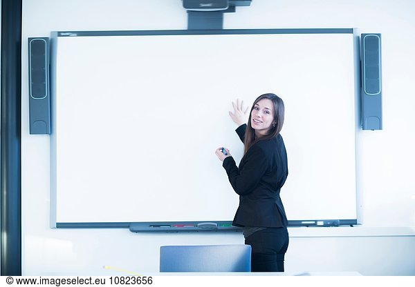 Young woman in office using whiteboard  looking over shoulder at camera smiling
