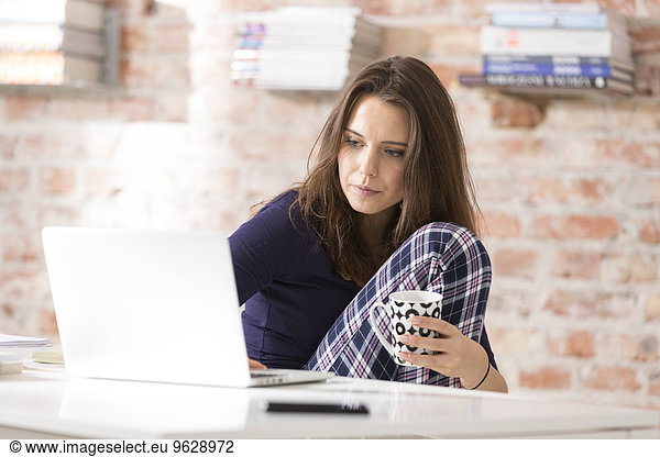 Young woman in pajamas using laptop