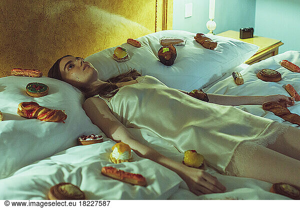 young woman in silk nightie lying on bed with many candies