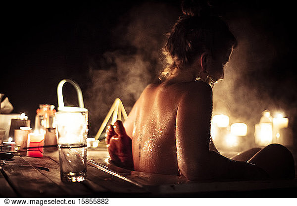 Young woman in steamy outdoor bath with partner by candle light