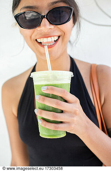 Young woman in sunglasses holding green juice