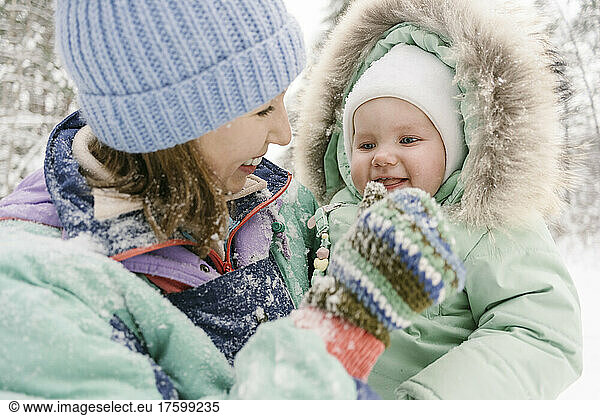Young woman in warm clothing playing with cute daughter in winter