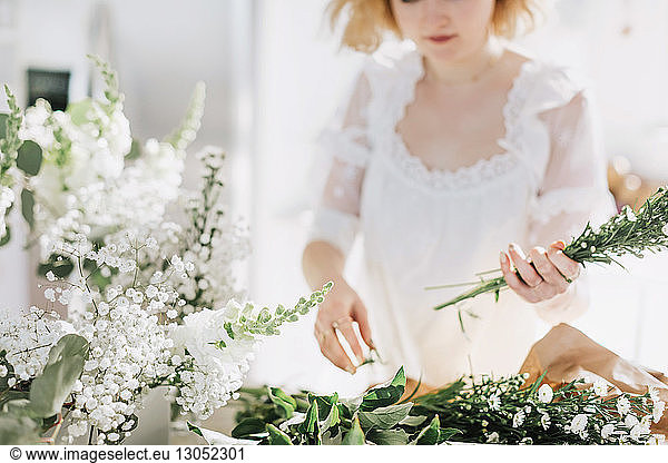 Young woman in white dress arranging white flowers  mid section