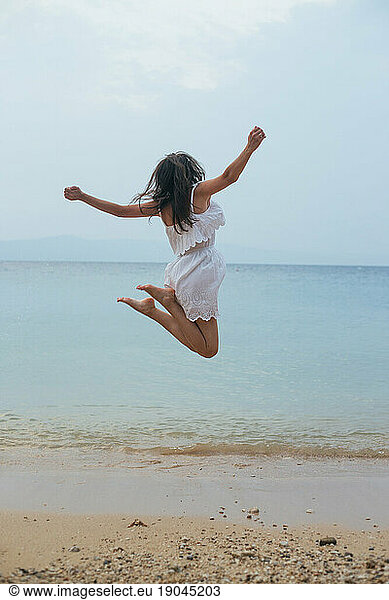 Young woman in white summer dress jumping on the beach