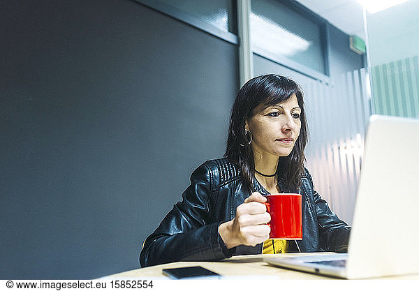 Young woman is drinking hot beverage at workplace.