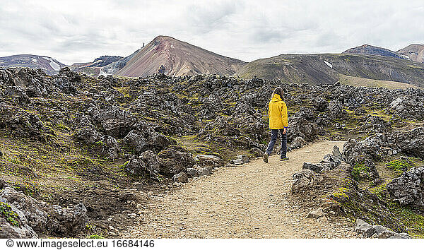 Young woman is hiking down Landmannalaugar rocky trail in Iceland