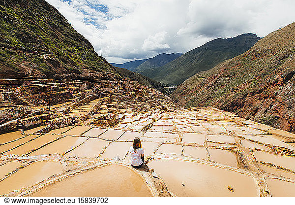 Young woman is sitting near the famous salt mines in Peru