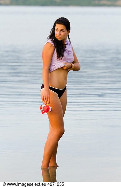 Young woman is standing in a shallow water with a toy fish in hand