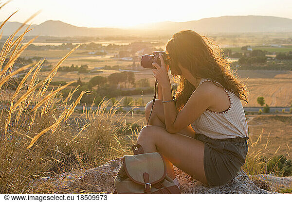 Young woman is taking a picture with her camera on top of a mountain