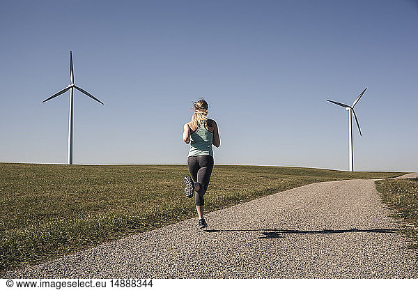 Young woman jogging on field way,  wind wheels in the background
