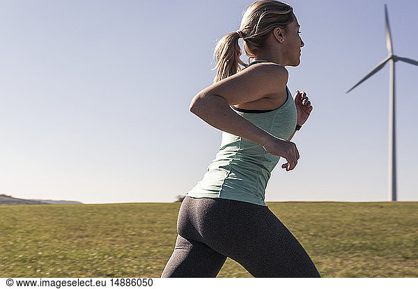 Young woman jogging on field way wind wheels in the background