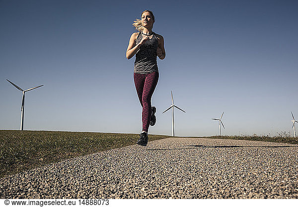 Young woman jogging on field way wind wheels in the background