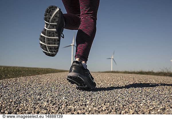 Young woman jogging on field way  wind wheels in the background