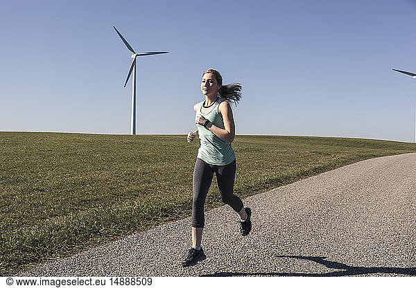 Young woman jogging on field way  wind wheels in the background