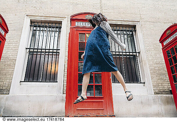 Young woman jumping in front of telephone booth