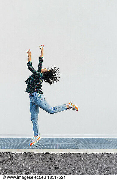 Young woman jumping in front of wall