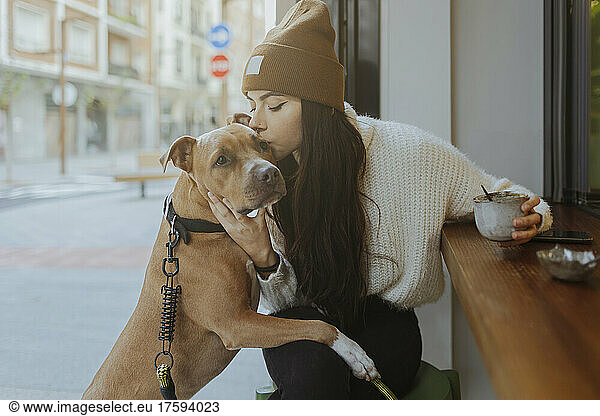 Young woman kissing dog sitting at sidewalk cafe