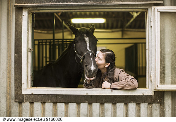 Young woman kissing horse in stable