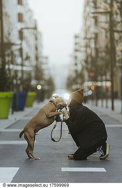 Young woman kissing playful dog on city street