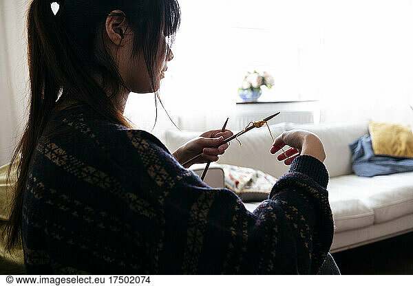 Young woman knitting wood with needle in living room