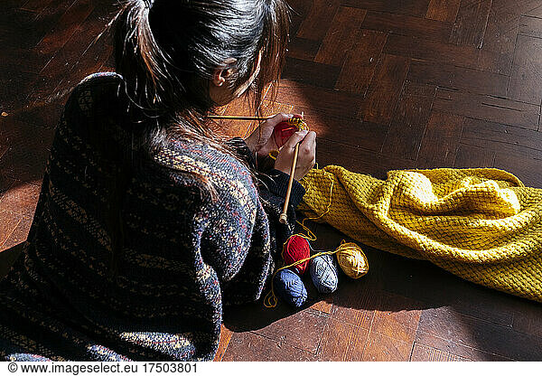 Young woman knitting wool on wooden floor at home