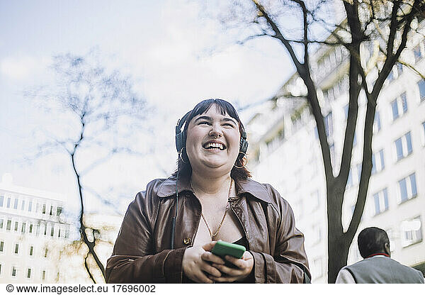 Young woman laughing while listening music through wireless headphones