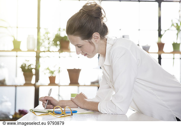 Young woman leaning at desk and writing