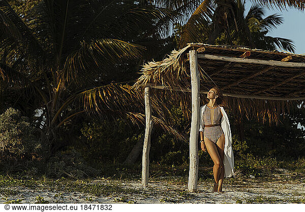 Young woman leaning at thatched canopy