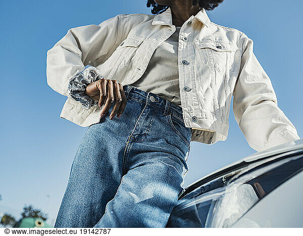 Young woman leaning on car headlight in front of sky